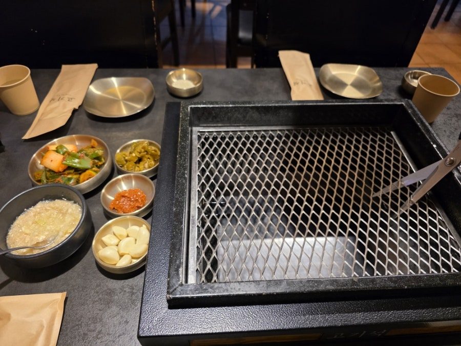 고기석 건대본점 불판 옆에 기본 반찬과 마늘 소스가 세팅된 테이블