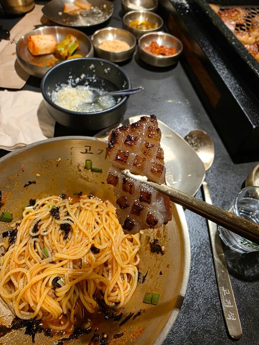비빔국수 위에 구운 벌집 양념 돼지껍데기를 든 모습