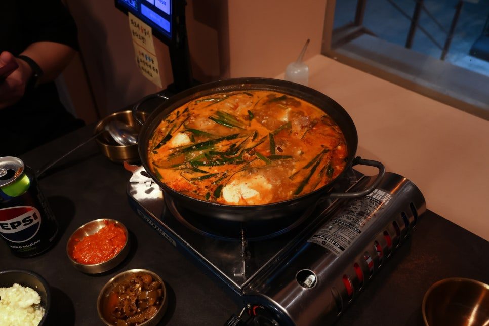 버너 위에서 끓는 얼큰 꽃게 순두부전골과 반찬, 음료 캔